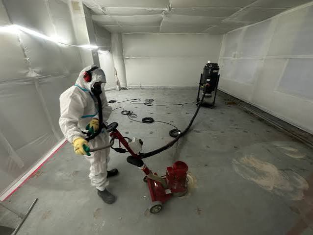 Opérateur réalisant un ponçage de sol sous aspiration HEPA dans une zone confinée